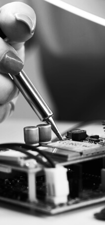 Black and white photo showing a hand using soldering iron on a circuit board